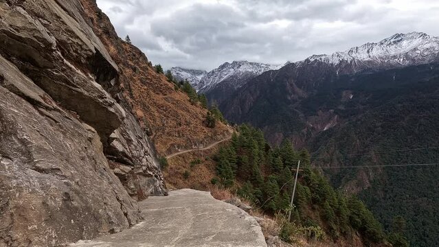 View along a mountain road with steep slopes to the side. Vast alpine valley with snowy mountains on the distant ridgel. Langtang Valley, Nepal