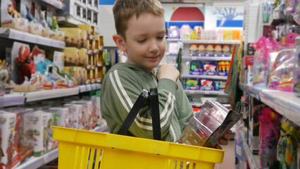 Close-up of a happy cute boy putting a toy into a shopping basket in a toy shop