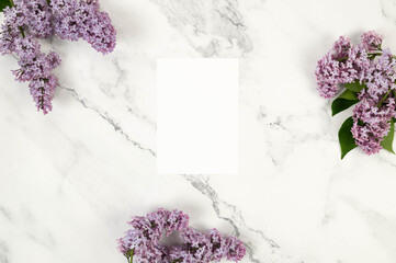Obraz premium Top view of purple lilac flowers on white marble background. White card, empty blank. Spring wallpaper, flat lay, copy space.