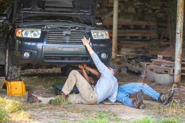 Father teaching son car repair auto mechanics under automobile. Interracial family.