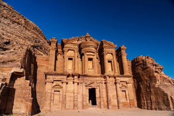 Impressive view of the ancient Al-Deir Monastery carved into the sandstone cliffs in Petra, Jordan, under a clear blue sky.