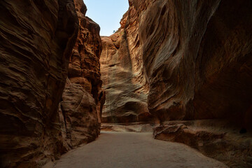View of the narrow Siq canyon pathway leading to Petra, Jordan, with towering sandstone cliffs. © Jirakul