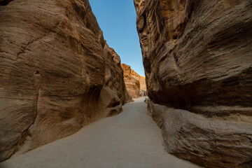 View of the narrow Siq canyon pathway leading to Petra, Jordan, with towering sandstone cliffs.