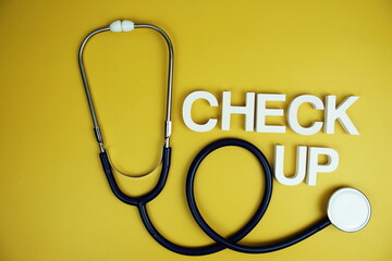 Stethoscope and Check up alphabet letters top view on yellow background