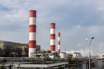 Red and white chimneys of a power plant with emissions, pipes, buildings and blue sky; chimneys of...