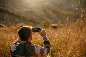 Man enjoying a hike in the rolling golden hills, backpack on his shoulders, and using a smartphone