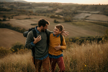 Cheerful teenage boy walking in nature with his dad, embracing, talking and smiling