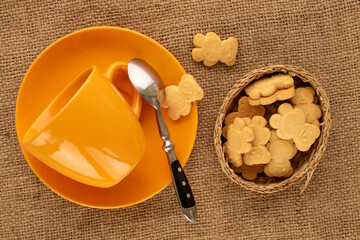 Delicious cookies in the shape of a bear with ceramic dishes on a jute cloth, top view, macro.