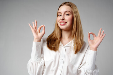 Young Woman Gesturing OK Sign With Hand Against a Neutral Background