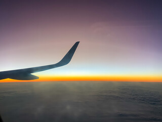 Wing of an airplane flying above the clouds at the time of sunset. Travel concept. Cloudscape