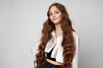 Confident Young Woman With Long Wavy Hair Posing in Casual Attire Against a Gray Backdrop
