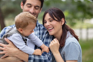 family walking in field carrying young baby son