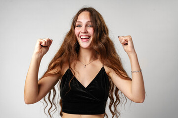 Young Woman Celebrating Victory With Raised Fists on a Plain Background