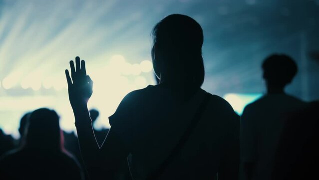 A woman raises her hands to worship God at a concert with colored lights. teenagers and many people happy hope slow motion