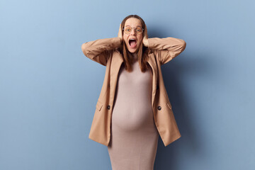 Despair confused excited pregnant woman wearing dress jacket and glasses isolated over blue...