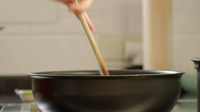 A woman's hand holds a wooden spoon with which she mixes the ingredients for the sofrito that is cooked inside a frying pan.