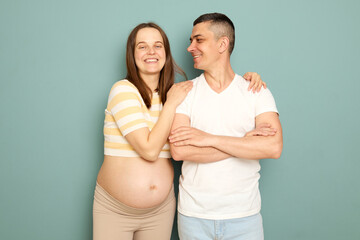 Cheerful pregnant woman hugging her husband looking at camera with smile happy family expecting...