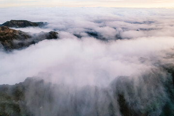 Aerial view of majestic mountain ridges at sunrise with falling fog from top of Pico do Areeiro, Madeira island, Portugal