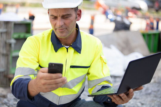 builder using a mobile phone and a laptop outdoors