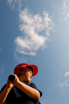 Young player in a red baseball helmet underneath a bright blue sky