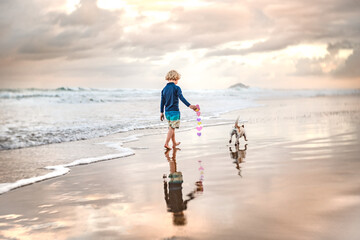 Child holding paper hearts walking on stunning beach with dog