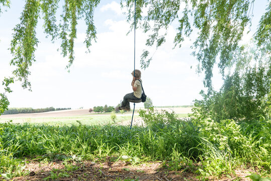 Young boy high on a rope swing under a willow tree