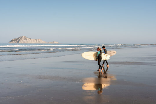 Two kids with surfboards at a beach in New Zealand