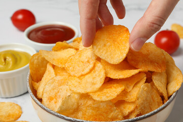 Potato chips in a bowl with sauce and tomatoes on a light background