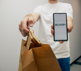 a courier in a white T-shirt and jeans holds a package made of recycled craft paper and a phone...