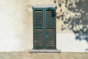 old teal shutters on a weathered window set against a textured white wall with dappled shadows