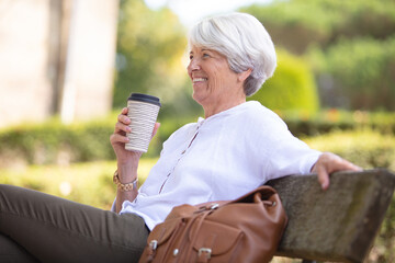 mature woman with cup of coffee on bench in park