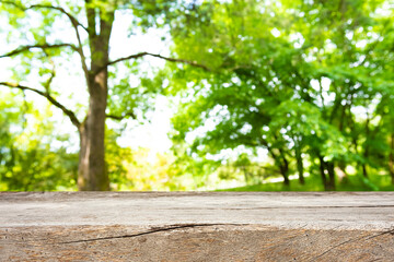 Aged wooden table top for product display on blurred nature green trees background