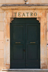 weathered green doors under a stone arch labeled 'TEATRO' in faded gold letters