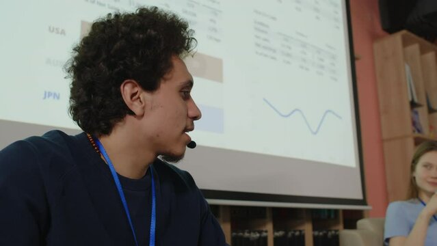 Gen Z middle eastern college student wearing wireless headset speaking into mic while giving presentation with female partner during educational conference