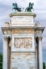 intricate triumphal arch topped with dynamic horse sculptures against a stormy sky