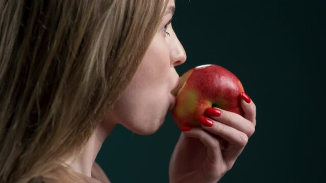 young beautiful well-groomed girl eats a red apple close-up, The lady eats an apple, chews it slowly, her whole face is not visible. mouth eats fruit. light snack