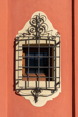 decorative wrought iron grill over window set in a coral painted wall with cream detailing