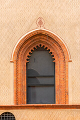 detailed gothic window framed with terracotta bricks on a patterned beige facade with elegant arch