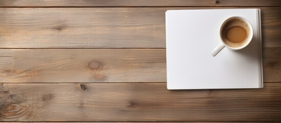 On a wooden table there is a cup of coffee and a notepad with ample copy space image