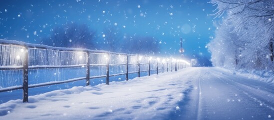 Fototapeta premium During winter a narrow road runs alongside a fence adorned with snow beacons for clear road visibility copy space image