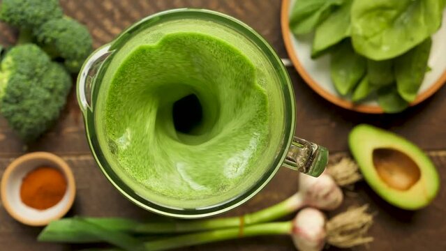 Blending a green vegetable smoothie using a blender with the lid open. Colorful green vegetable smoothie with broccoli, avocado and spinach with garlic. Healthy food vegetarian diet. Top view, table