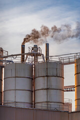 Polluting black smoke coming out of chimneys next to some warehouses in a large industry, environmental pollution.