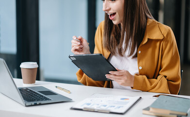 Young beautiful woman typing on tablet and laptop while sitting at the working white table in office