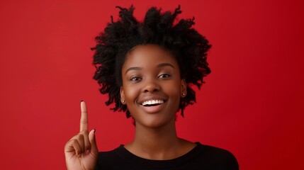 Portrait of beautiful young black woman in yellow top with short afro hair, smiling and pointing up on a red background, template for advertising or promotion, with copy space for text