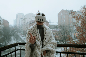 Immersed in virtual reality, a girl wears a VR headset on the balcony during winter.