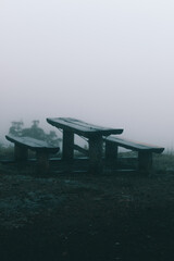 Wooden benches and table soaked wet from the rainy weather and background foggy view with no people around.