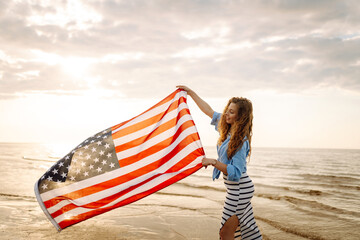 Young woman holding national American flag cover ocean beach holiday travel at summer romantic sunset. America independence day concept. 4th of July.