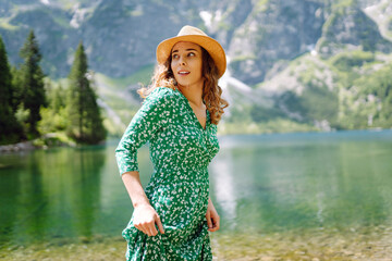 Young woman in summer dress enjoying beauty of nature looking at mountain lake. Adventure travel in Slovenia, Europe.  Scenery of the majestic mountains.
