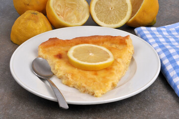 Part de tarte au citron dans une assiette avec une cuillère et des citrons au second plan