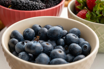 Close-up view of blueberries, strawberries and black mulberries in fruit cups on a marble surface